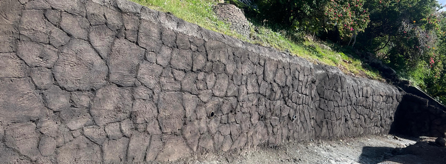 Finished sculpted shotcrete rock retaining wall supporting a landscaped slope