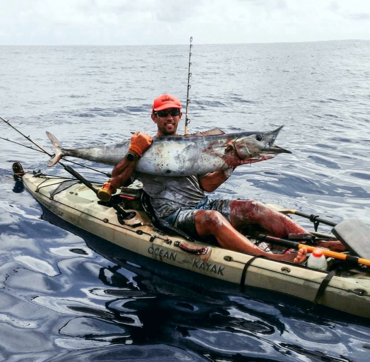 Isaac holding his catch while seated in his kayak on the ocean