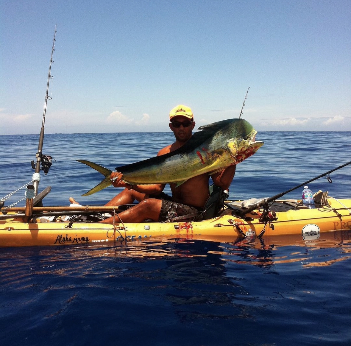 Isaac holding a mahi-mahi in his yellow kayak on open water